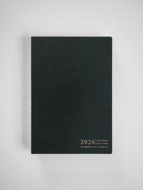 Deep charcoal A5 compact planner cover featuring centrally embossed gold lettering for "2026 A5 V. Compact Full Year Common Planner."