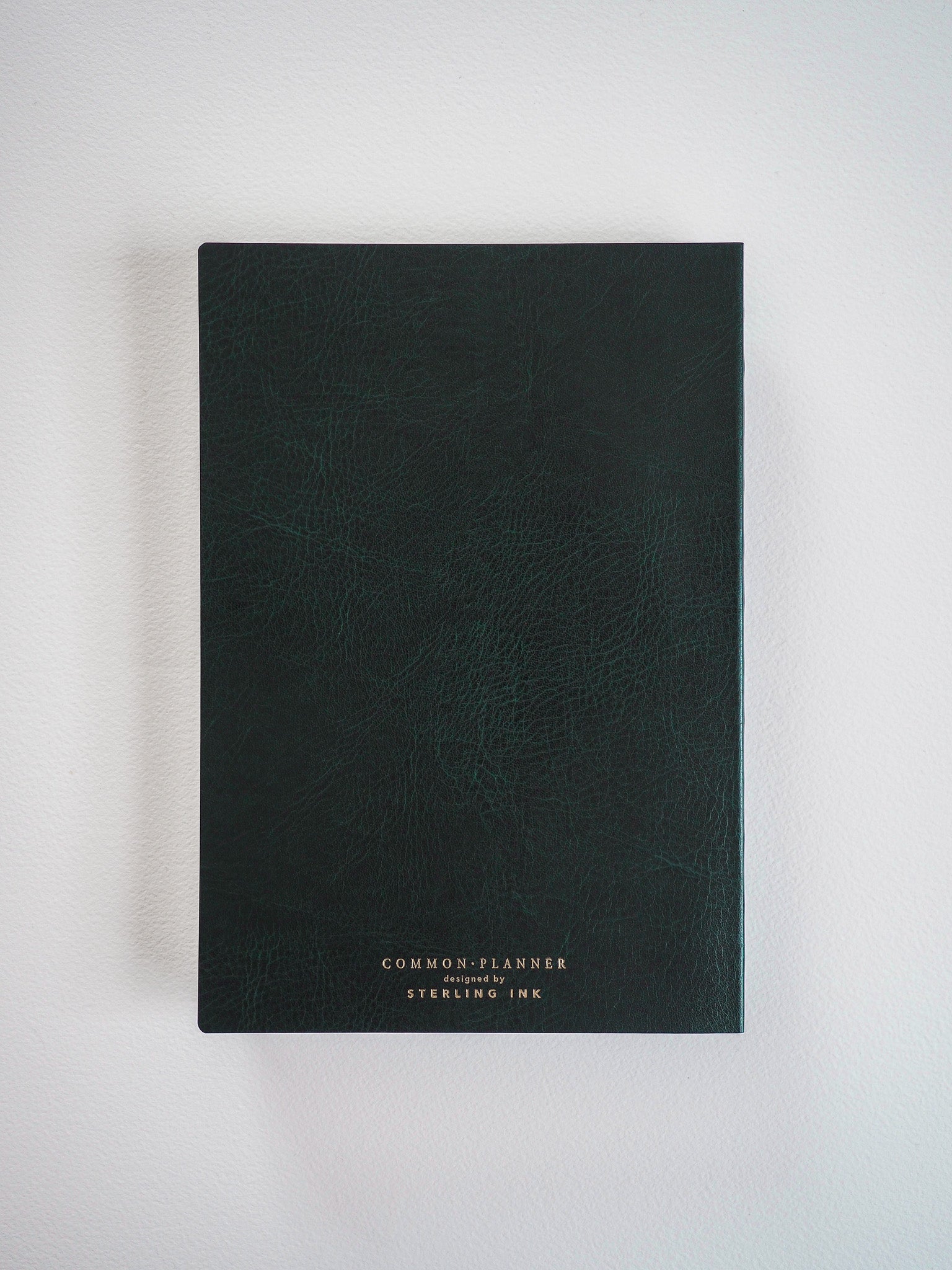 A compact A5 vertical planner with a deep matte green cover, subtly branded with "Common Planner designed by Sterling Ink."