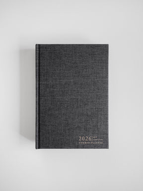 Dark charcoal A5 planner featuring a subtle linen texture and minimalist front design, prominently displaying the year 2026 and the Common Planner logo.