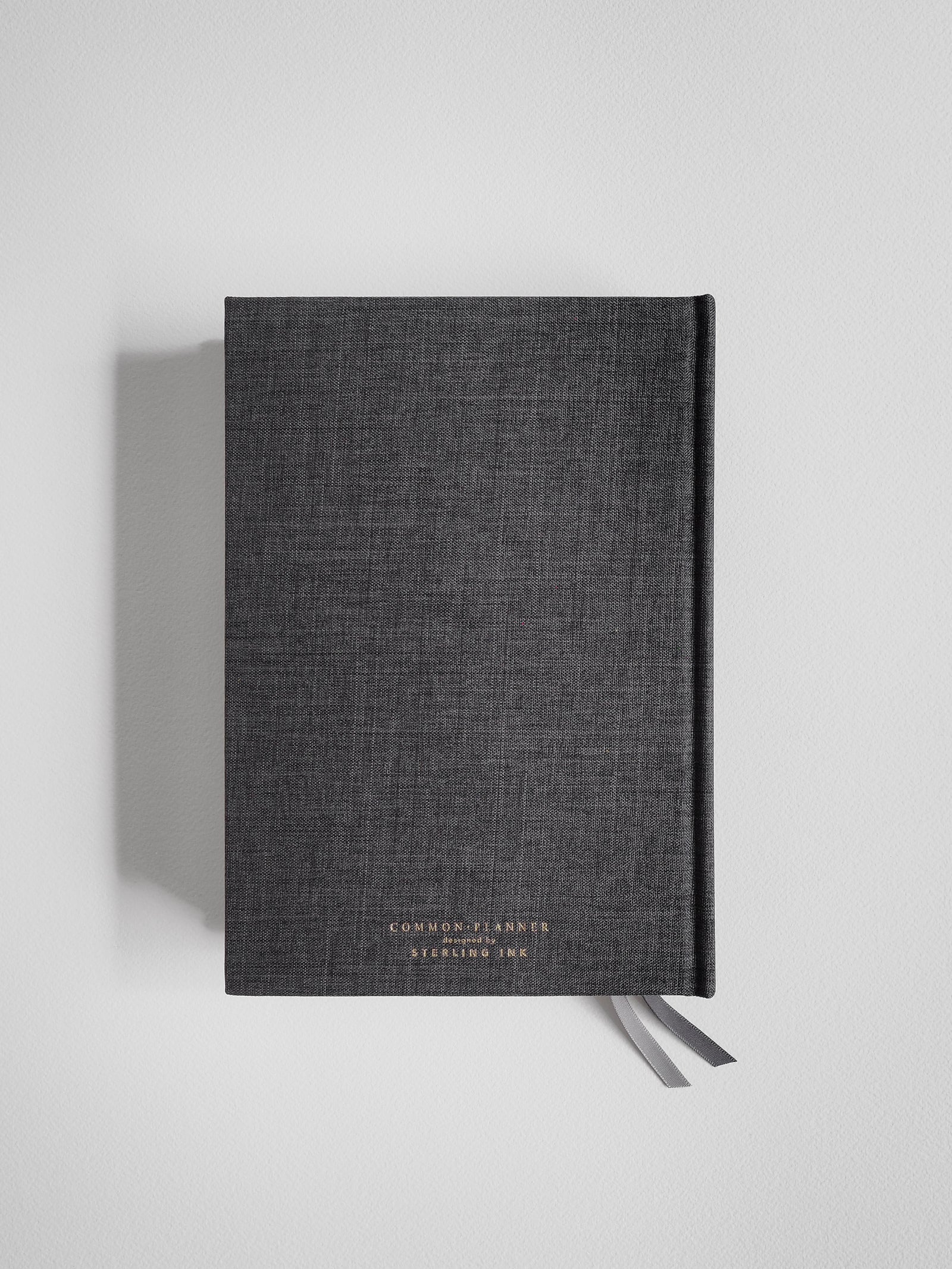 A dark charcoal A5 planner featuring subtle, minimalist branding and centered typography reading "Common Planner" and "Designed by Stealing Ink."