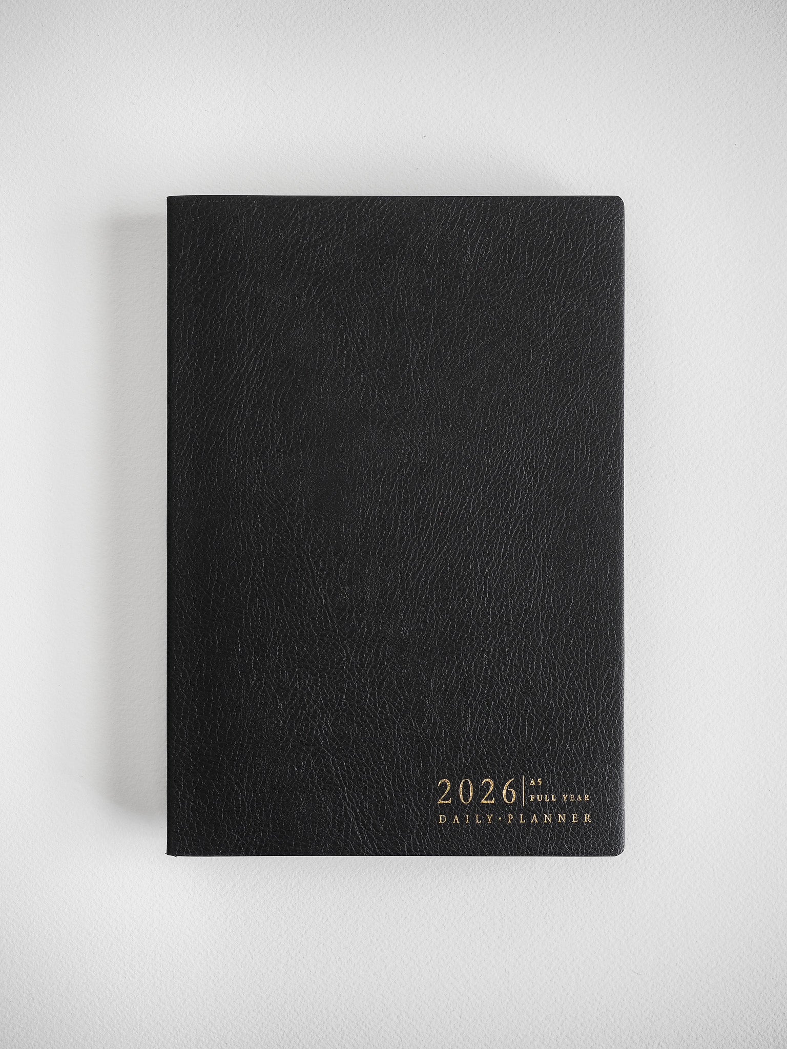 Black A5 daily planner with a textured, matte cover and gold foil embossing of "2026 Full Year Daily Planner."