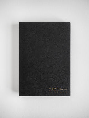 Black A5 daily planner with a textured, matte cover and gold foil embossing of "2026 Full Year Daily Planner."