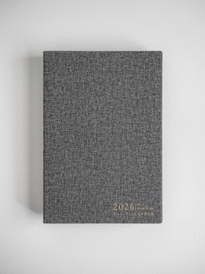 Minimalist A5 daily planner featuring a heather gray, textured cover and discreetly embossed text reading "2026 Daily Planner."