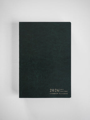 Deep forest green A5 planner with a textured, synthetic leather cover displaying the embossed title "2026 Full Year Common Planner."
