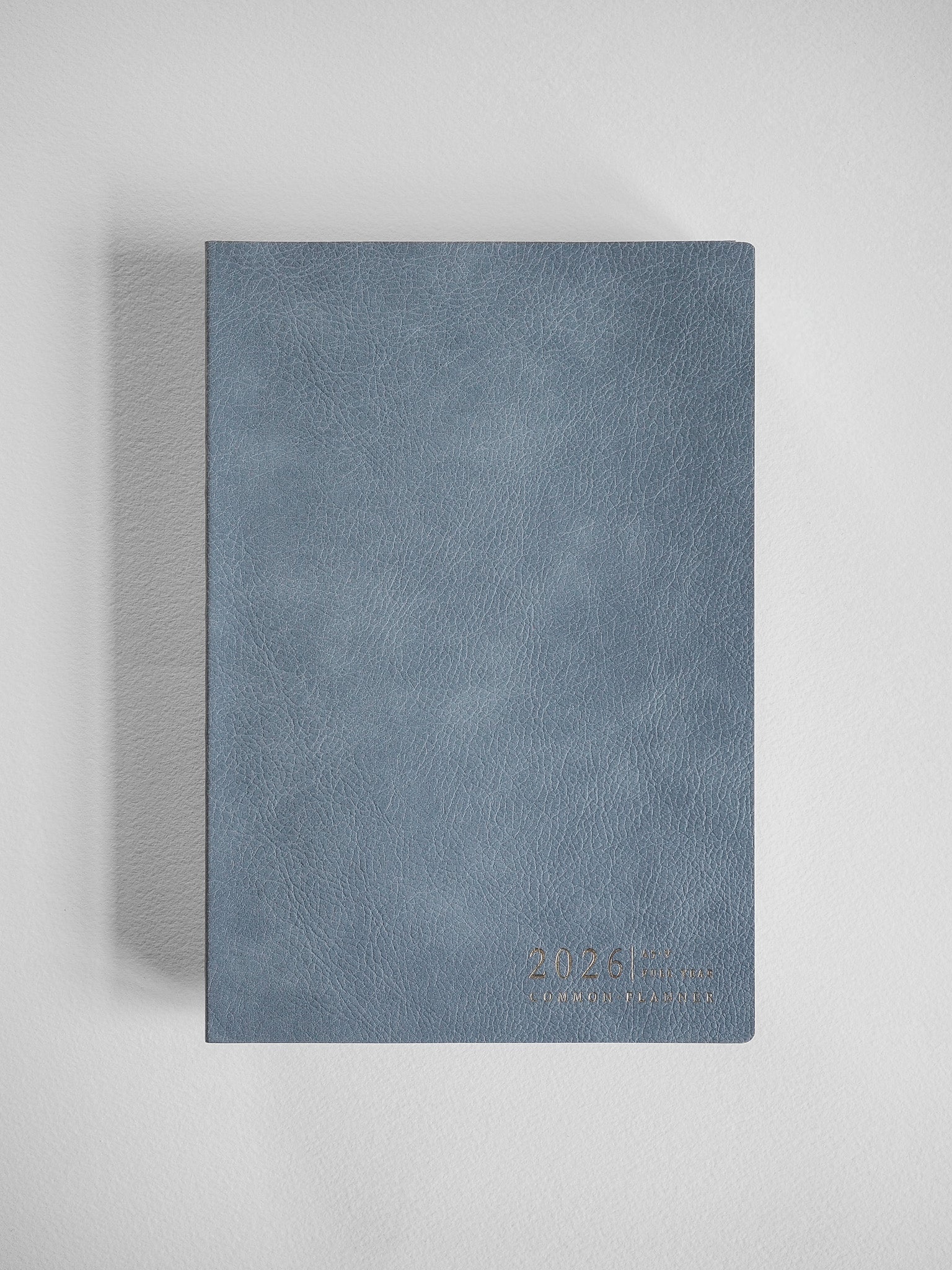 A textured, vertical A5 planner cover in slate blue, featuring a simple embossed design with the '2026 Common Planner' text.
