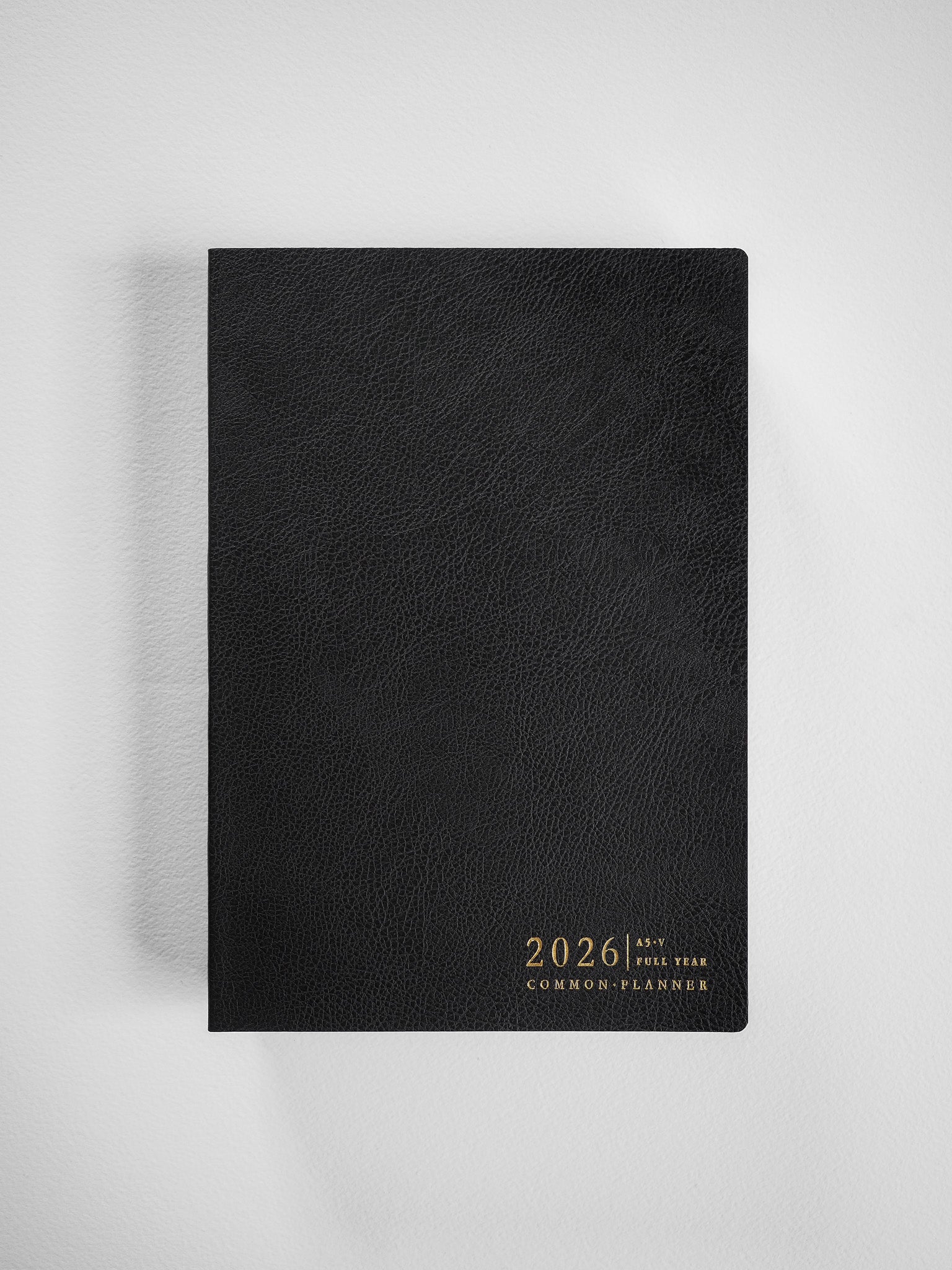 Minimalist A5 vertical planner with a black textured cover and elegant gold foil stamping, featuring the text "2026 Common Planner" for organized scheduling.
