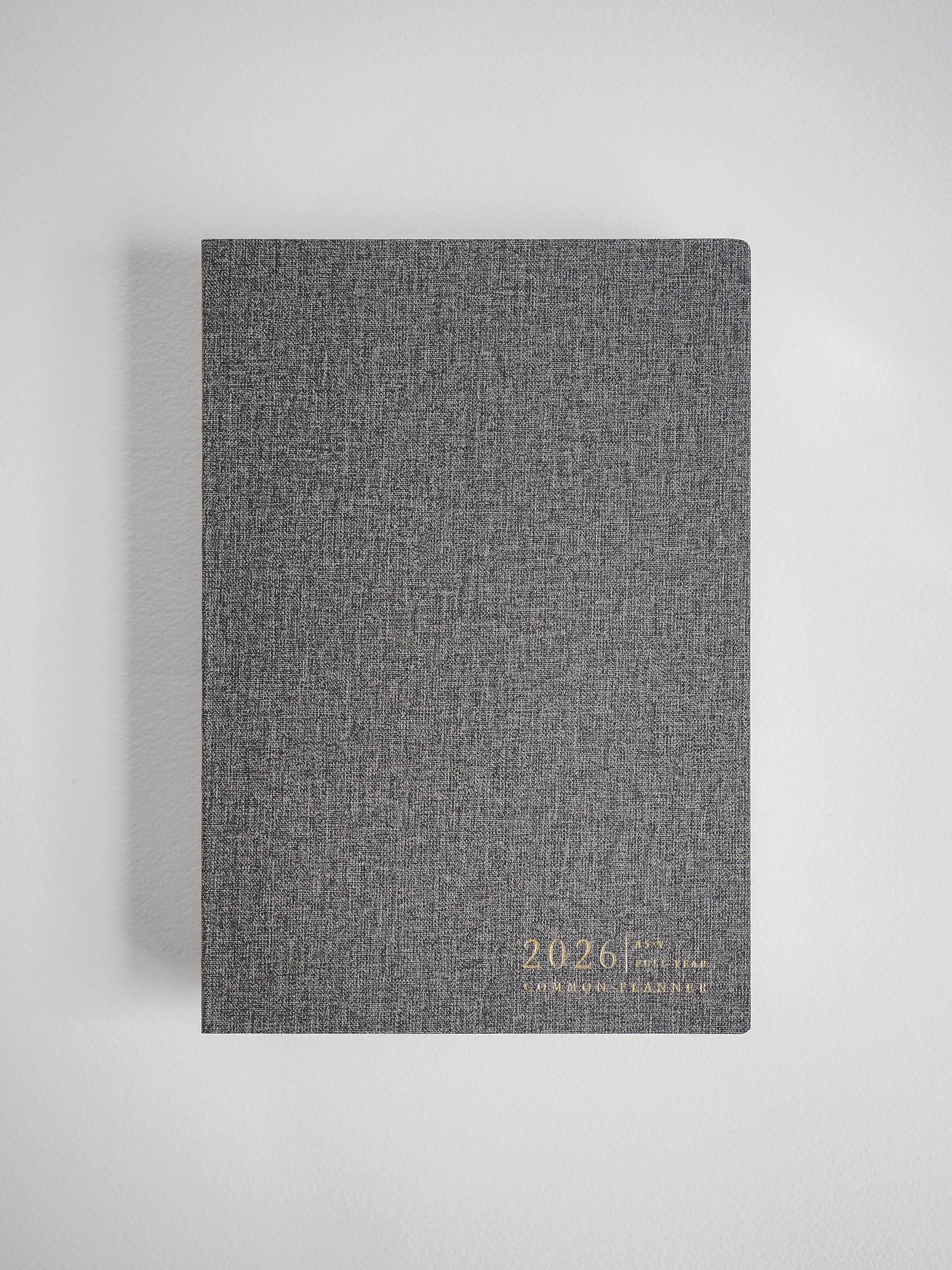 Minimalist A5 vertical planner cover in charcoal gray linen texture, displaying the embossed year 2026 and brand logo.