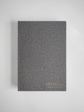 Minimalist A5 vertical planner cover in charcoal gray linen texture, displaying the embossed year 2026 and brand logo.