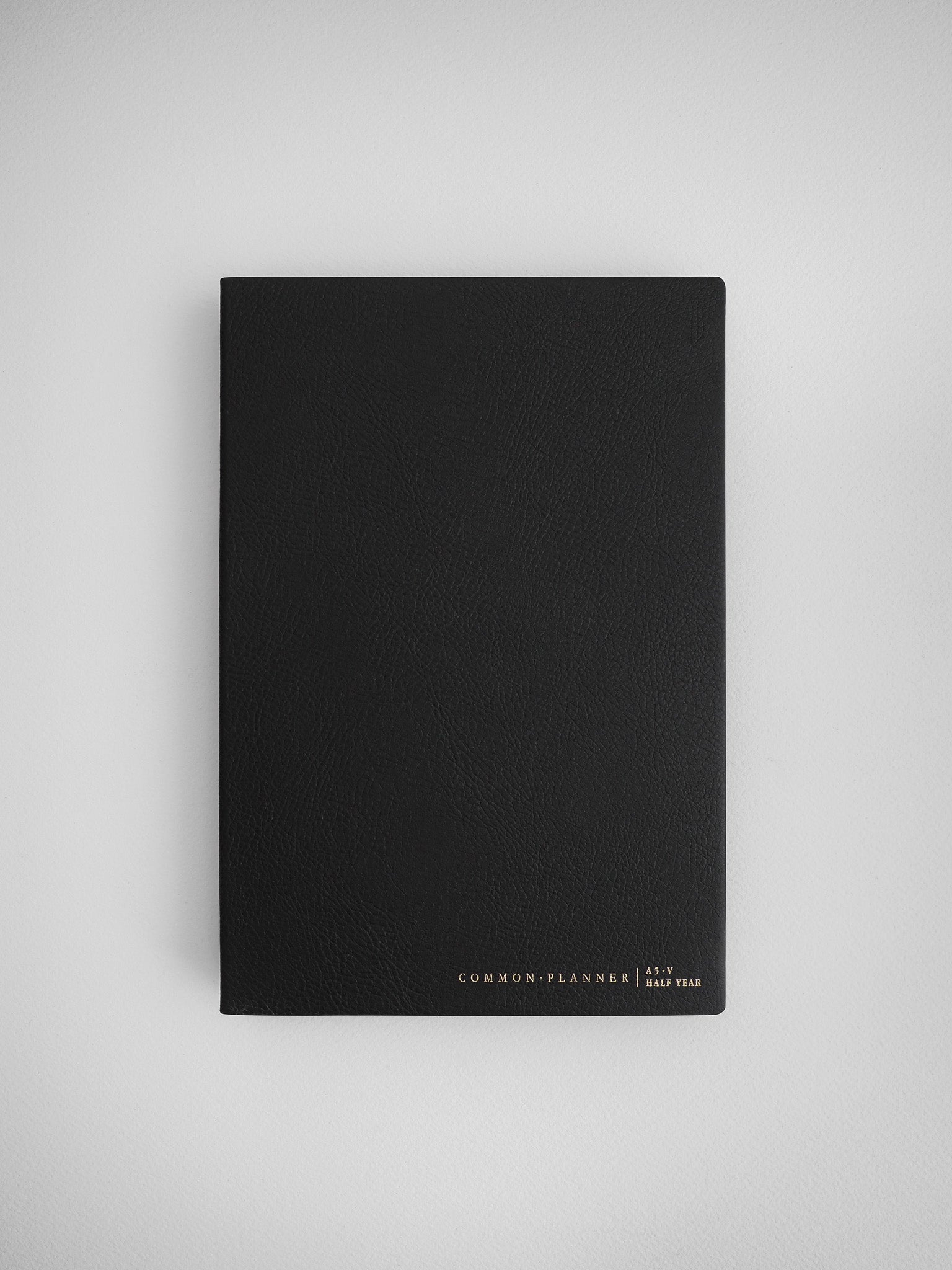 Sleek black A5 planner with a matte cover, labeled "Common Planner | Half Year," making it an elegant and minimal stationery item for planning and journaling.