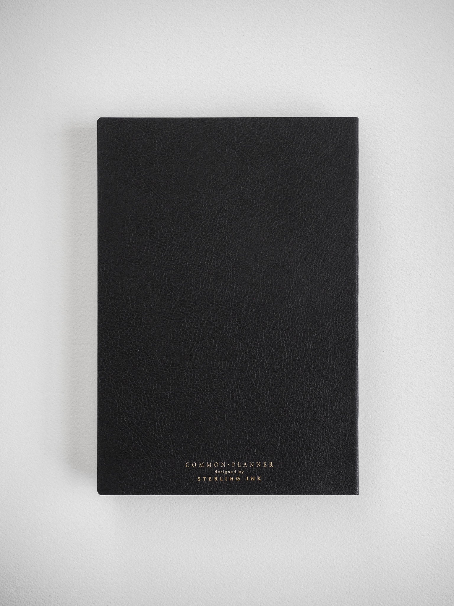 Minimalist black planner bound in faux leather, featuring centralized gold foil stamping that reads "COMMON PLANNER by STERLING INK."