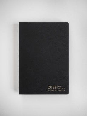 Sleek black A5 planner with a structured cover featuring gold lettering that reads "2026 A5-V Part Two Common Planner."