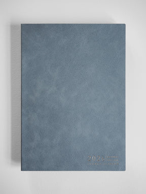 Elegant slate blue B5 planner with a subtle faux-leather texture, embossed with the year 2026, ready for writing and organization.