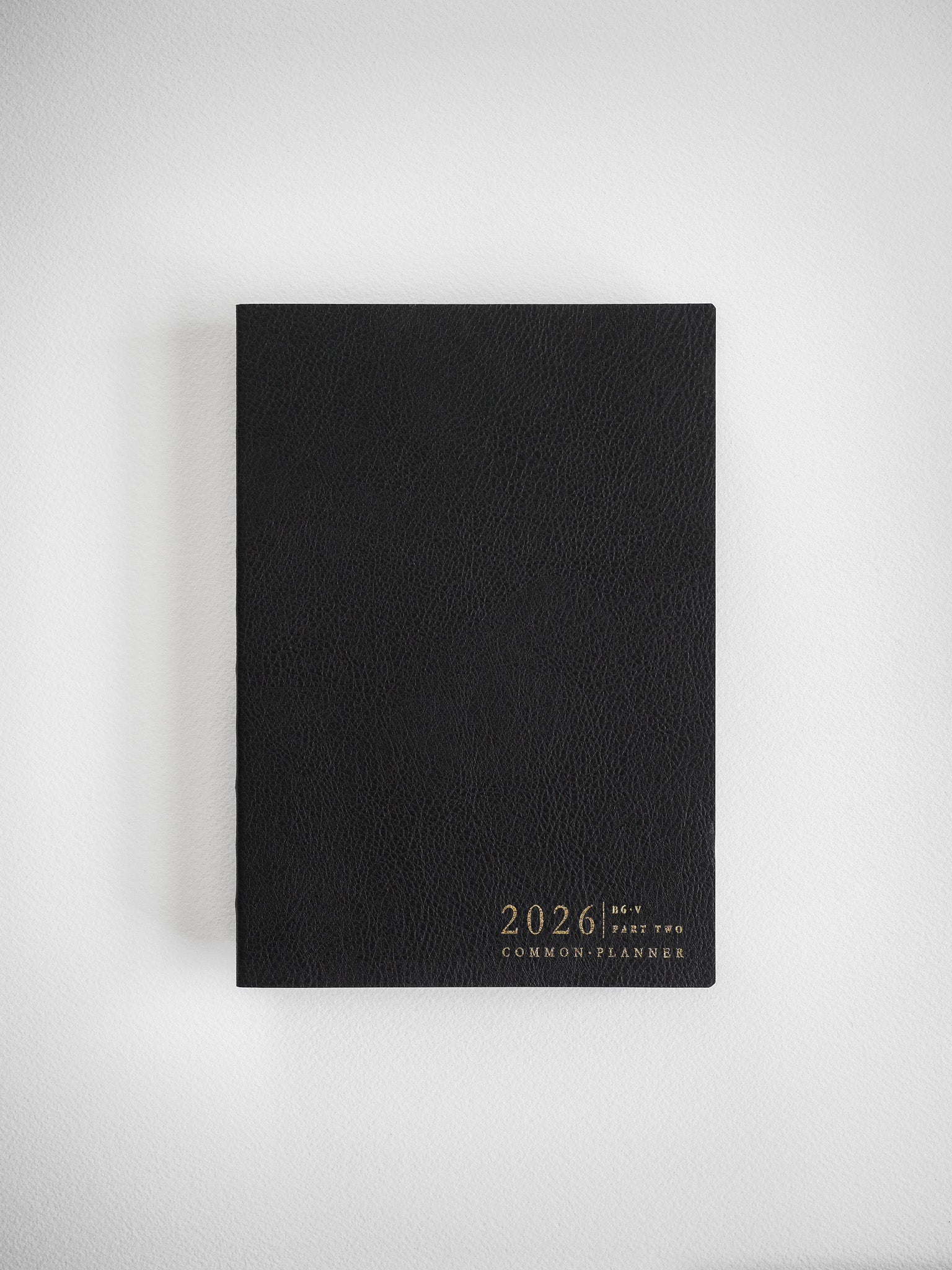 Sleek matte black B6 vertical planner cover adorned with sophisticated gold metallic foil lettering announcing the 2026 Common Planner.