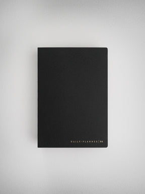 Sleek, solid black B6 daily planner notebook, featuring minimalist design and subtle metallic gold foil branding.