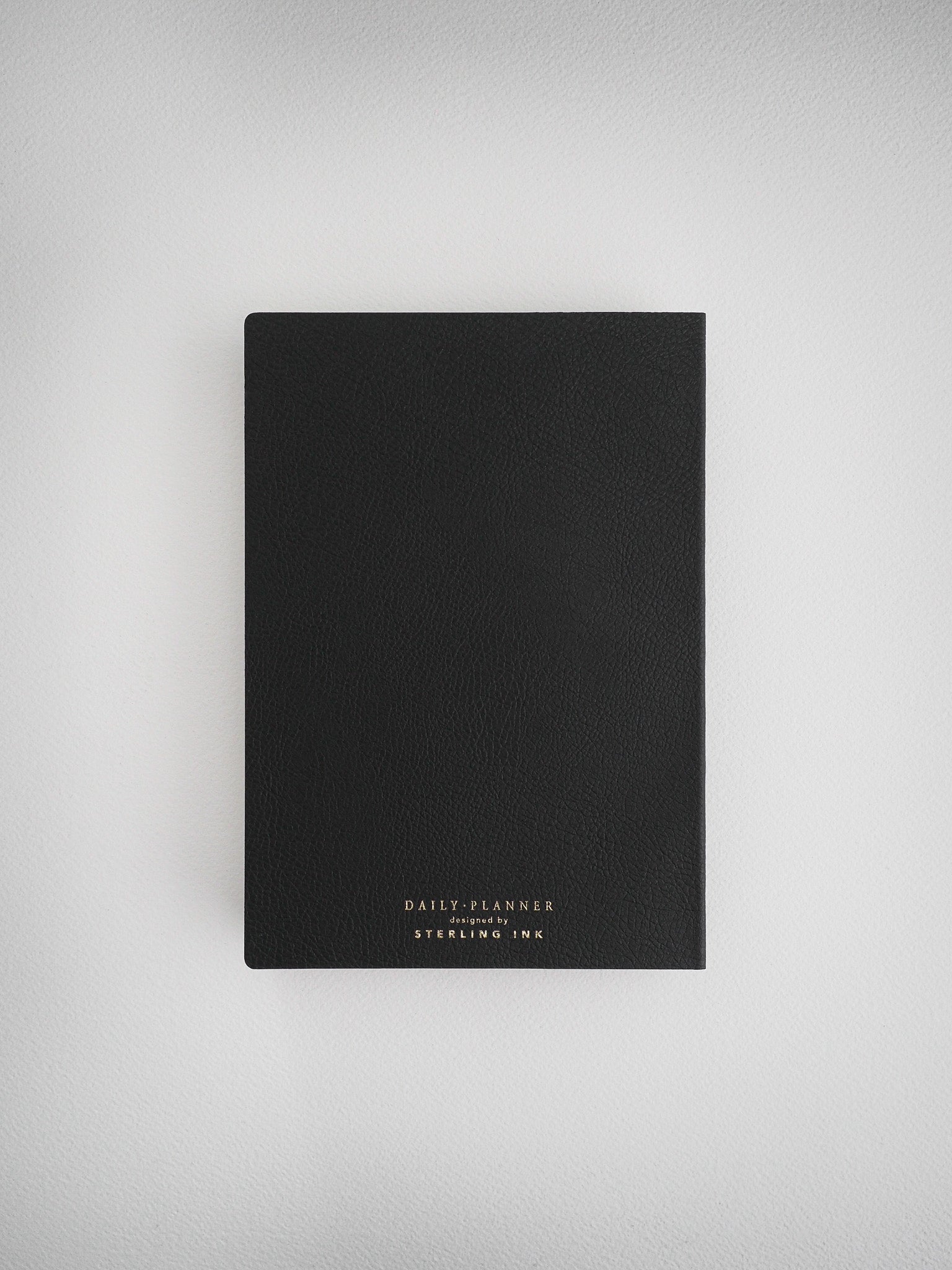 Minimalist black daily planner notebook designed for undated use, featuring elegant white branding from Sterling Ink for an organized look.