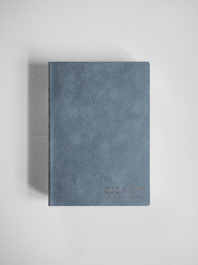 Slate blue, textured B6 planner for 2026, featuring a compact, horizontal format with subtle year branding printed near the bottom.