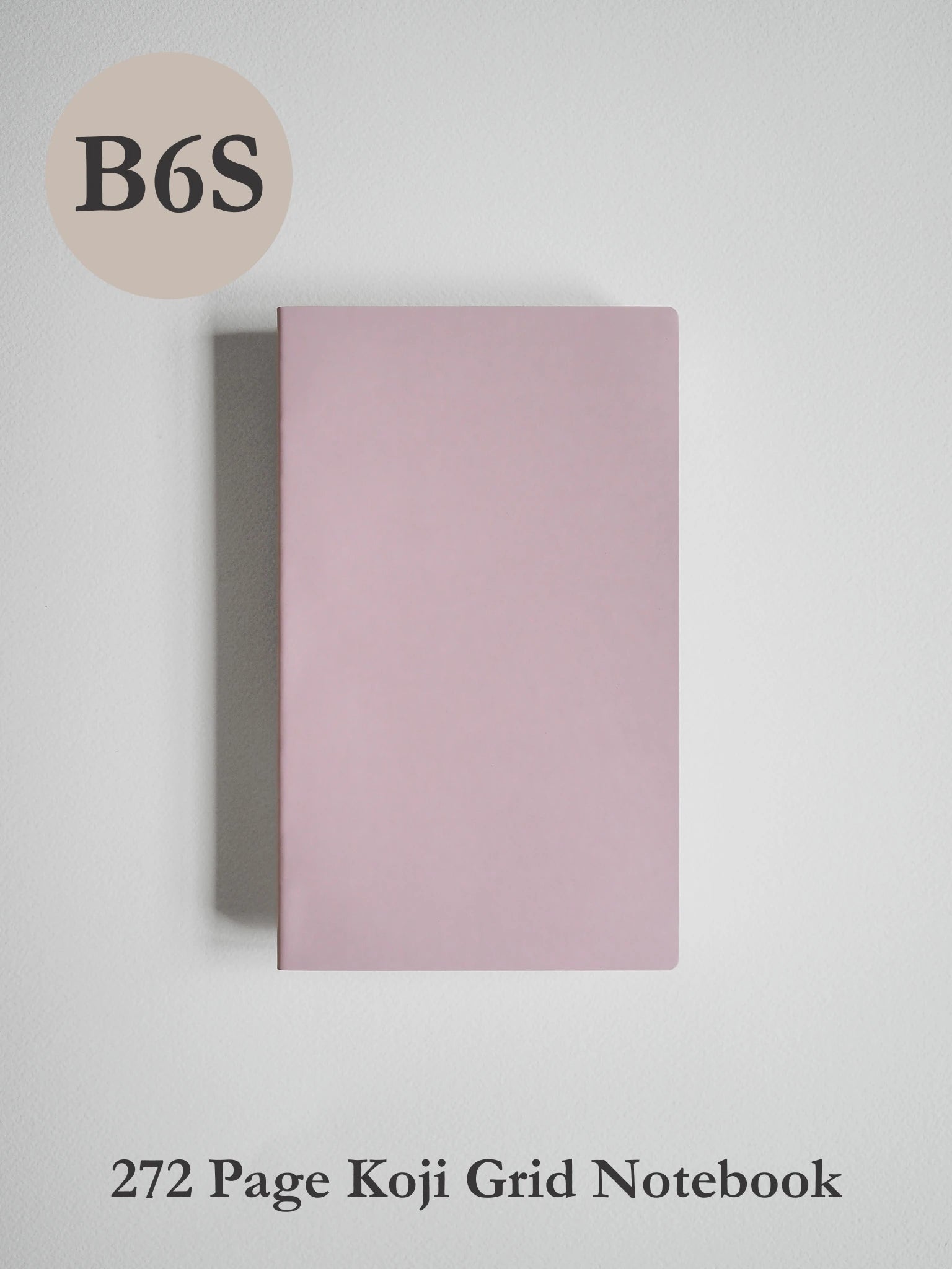 A minimalist pink notebook with a grid layout, shown closed on a light gray background. Text overlays indicate 'B6S' in a beige circle at the top left and '272 Page Koji Grid Notebook' at the bottom.
#Color_Fairyfloss