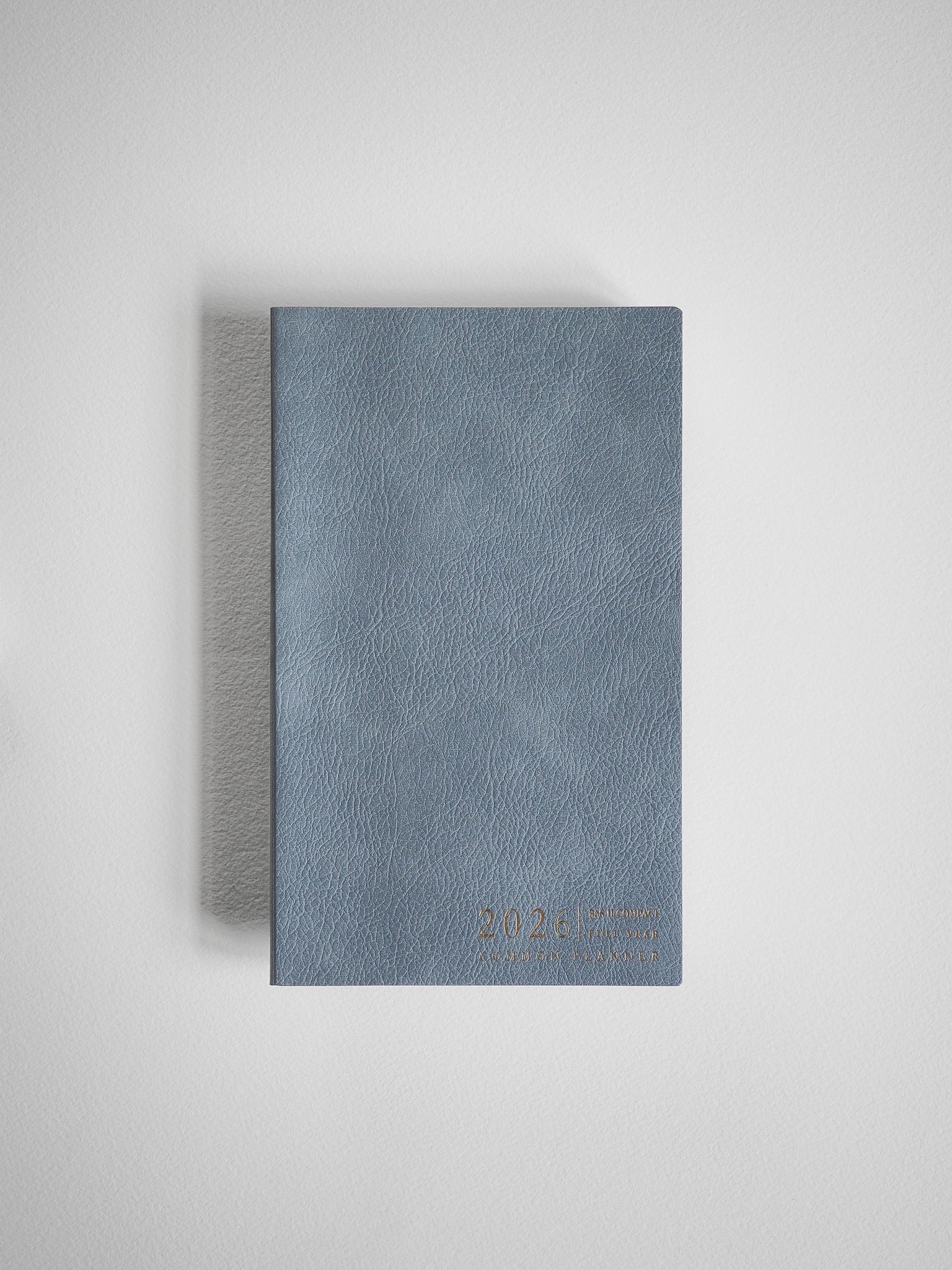 Compact B6 planner featuring a matte, slate blue textured faux leather cover with discreetly embossed year text.