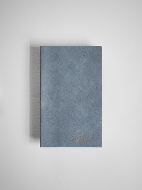 Compact B6 planner featuring a matte, slate blue textured faux leather cover with discreetly embossed year text.