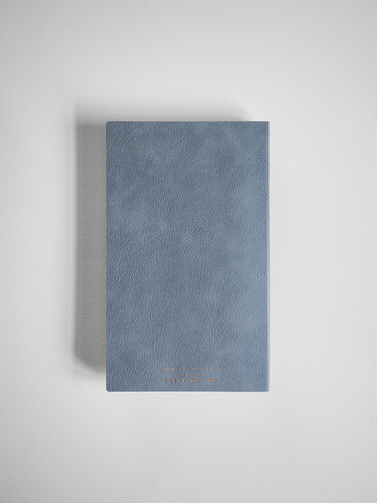 Muted slate blue B6 planner with a textured, compact cover and elegant gold embossed branding, perfect for tracking your 2026 full year schedule.