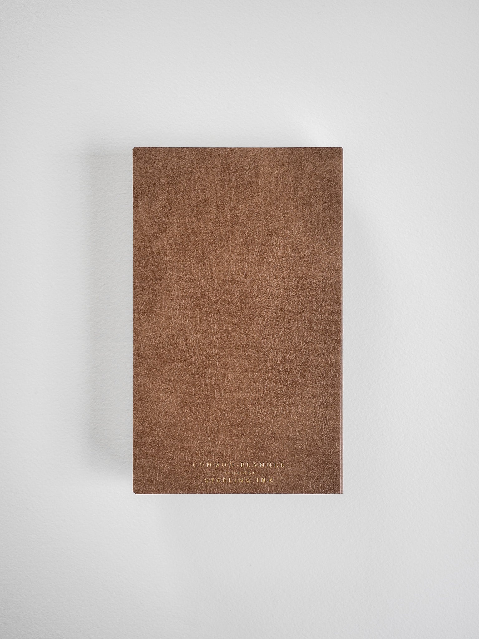 Rich cognac brown B6 planner with a minimalist, solid cover featuring debossed text reading "COMMON PLANNER" and "STERLING INK."