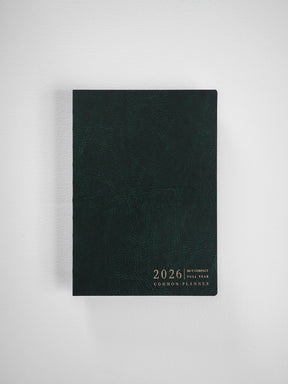 Minimalist dark forest green planner cover with embossed texture, featuring clean white typography detailing "2026 B6 Vertical Compact Full Year Common Planner."