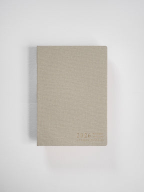 Compact B6 vertical planner with a textured beige cover, featuring subtle, minimalist debossed lettering for "2026 Common Planner."