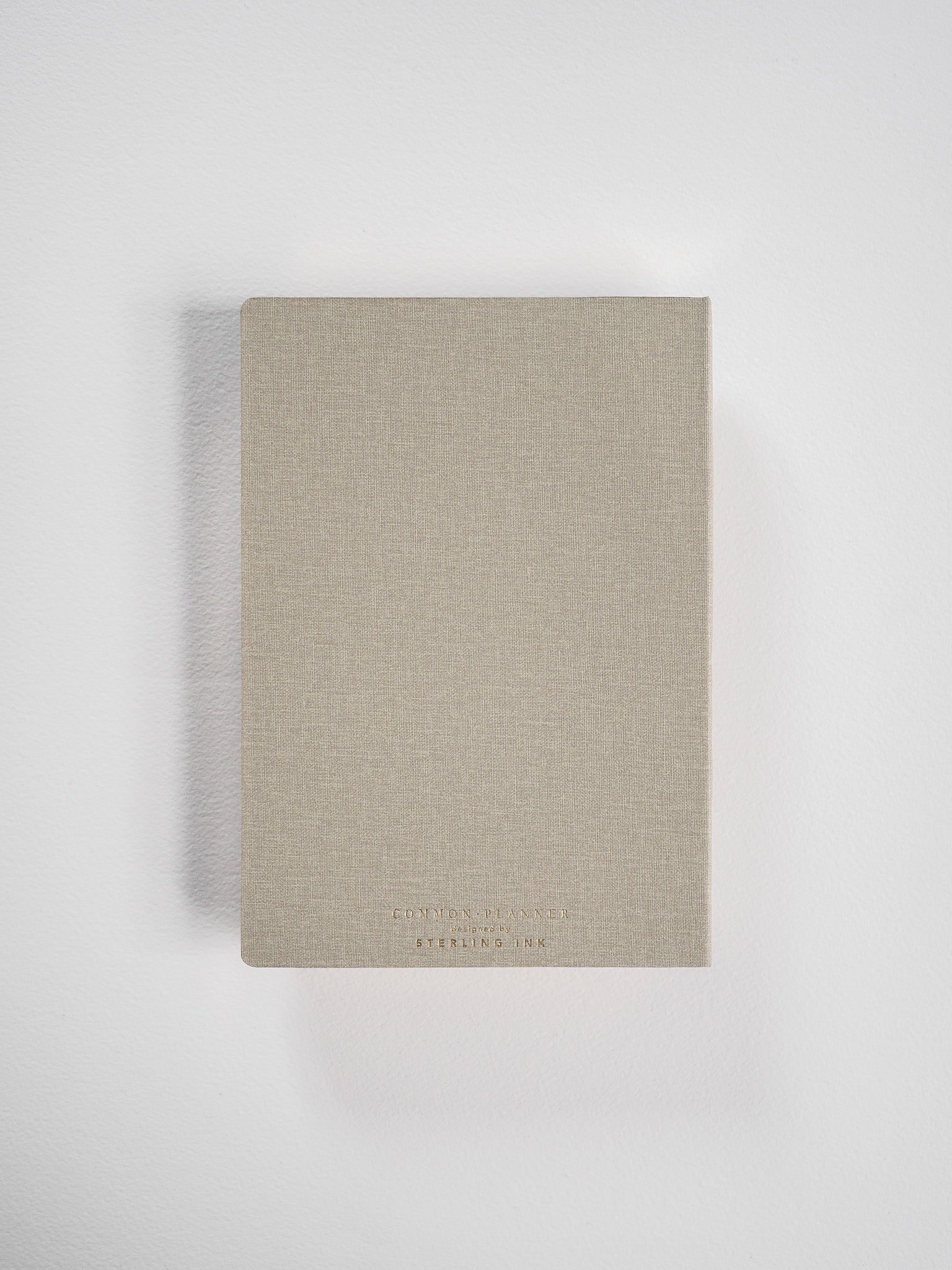A compact B6 vertical planner bound in solid light beige cardstock, featuring minimal centered black branding text for the Common Planner 2026.