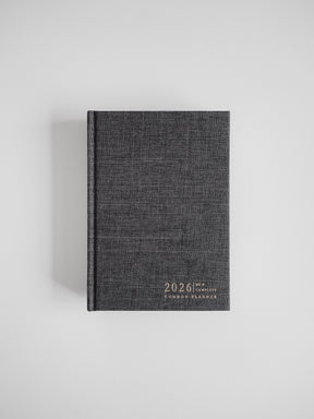 A dark charcoal B6 planner bound in textured material, featuring the embossed and centered title "2026 Common Planner" on the front cover.