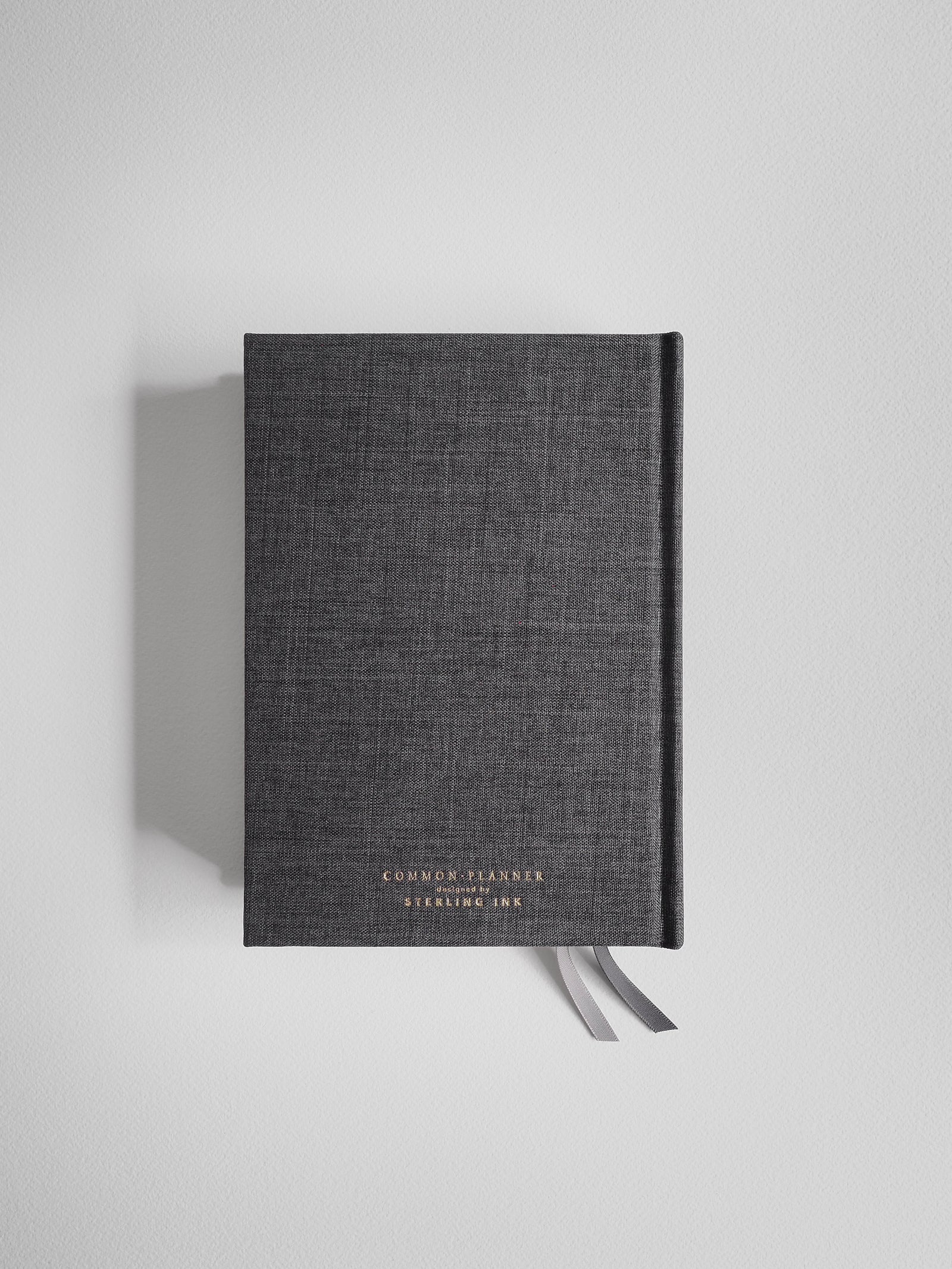 Dark gray B6 planner journal with a subtle textured cover, prominently featuring the gold-lettering title "Common Planner" and "Designed by Sterling Ink."