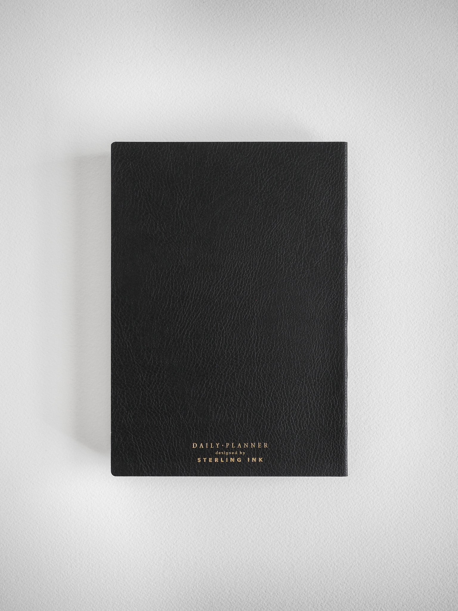Sleek black daily planner with a sophisticated faux leather cover and subtle gold lettering that spells out "DAILY PLANNER designed by STERLING INK."