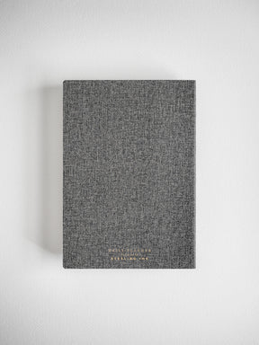 Dark charcoal B6 daily planner with a woven, heathered cover texture and elegant gold foil branding for organizing the year 2026.