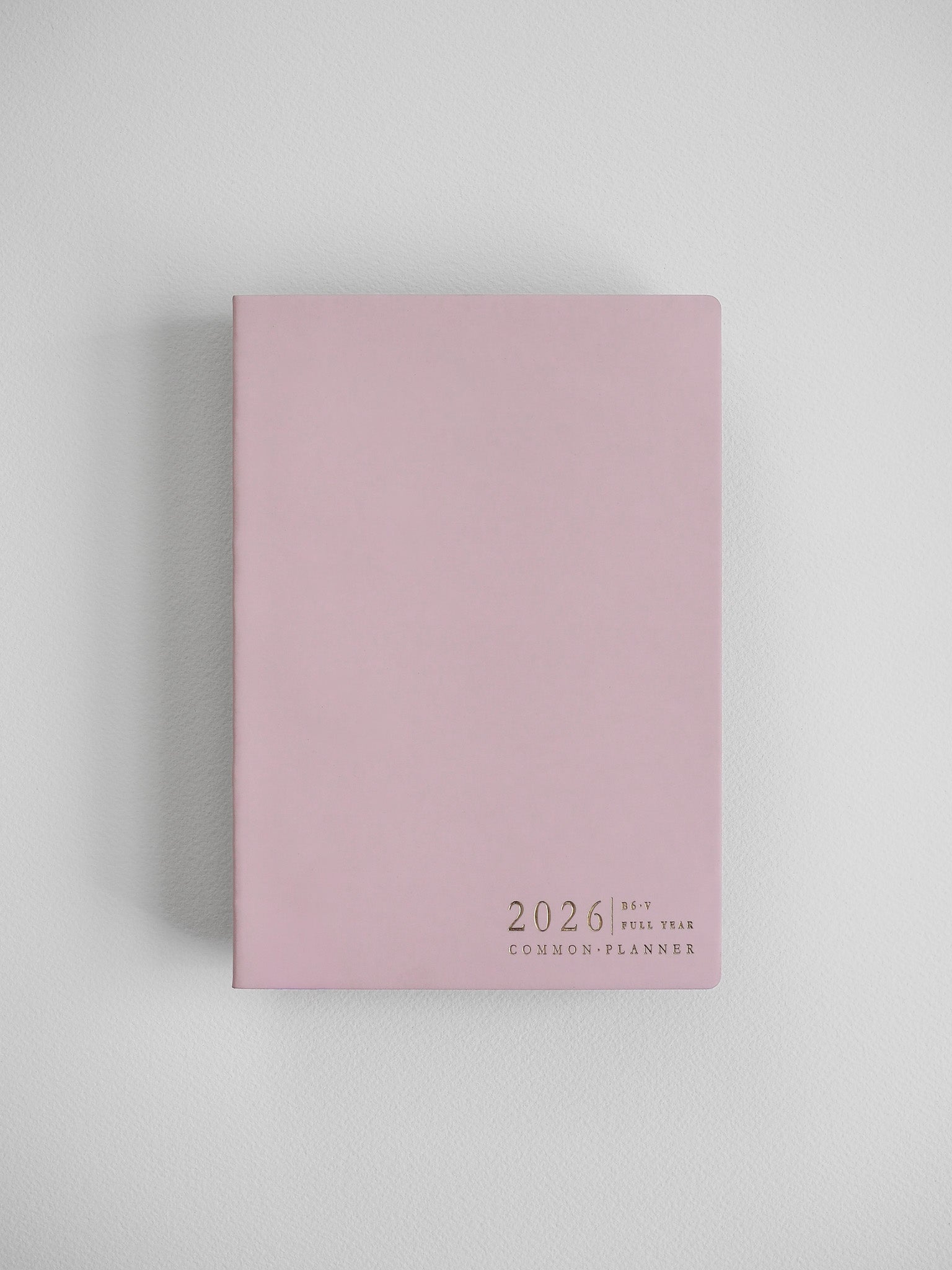 The minimalist B6 vertical planner features a soft blush pink cover with centered black typography that reads "2026 Full Year Common Planner."