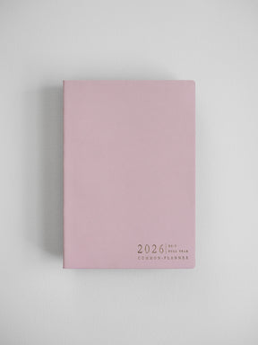 The minimalist B6 vertical planner features a soft blush pink cover with centered black typography that reads "2026 Full Year Common Planner."