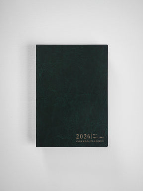 Deep forest green planner with a textured, faux leather cover, featuring centered gold lettering that reads "2026 Full Year Common Planner."