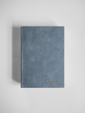 Minimalist B6 vertical full year planner with a textured, muted dusty blue cover, featuring discreet 2026 branding.