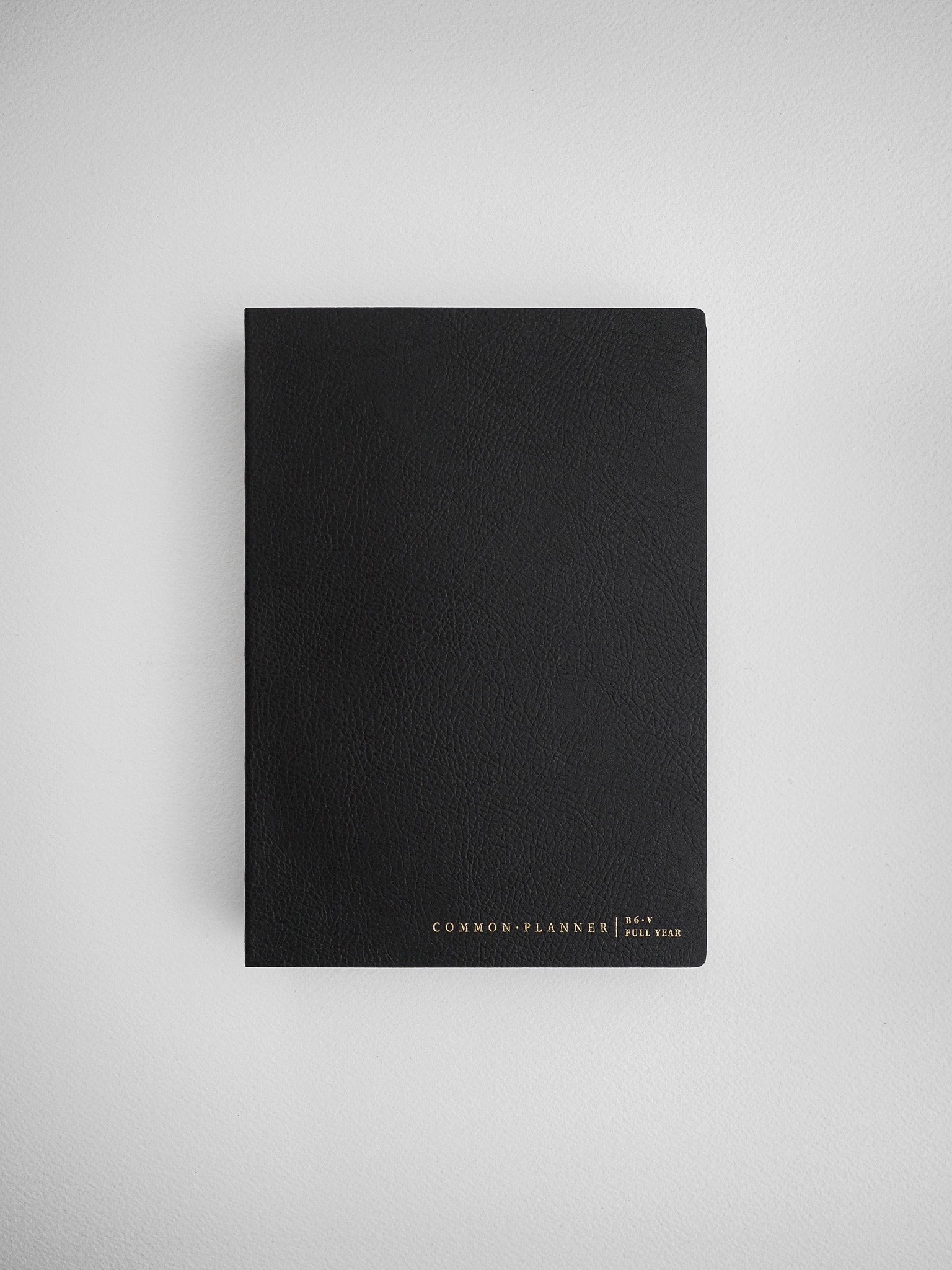 Minimalist black B6 vertical planner cover featuring subtle white lettering that reads "COMMON PLANNER | B6 V FULL YEAR."