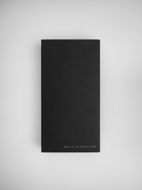 Minimalist black daily planner journal with a smooth faux leather cover and subtle "DAILY PLANNER N1" embossed branding.