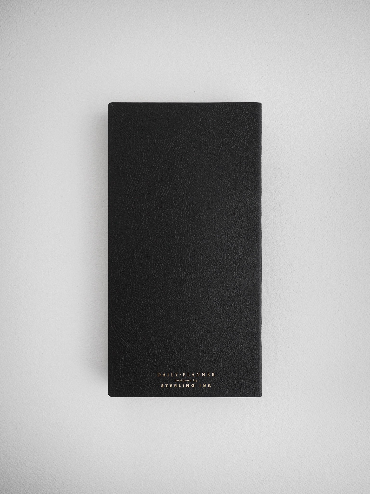 Sleek, solid black undated daily planner journal featuring a minimalist design and white branding for "Daily Planner" by Sterling Ink.