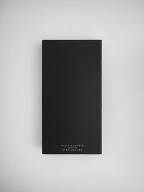 Sleek, solid black undated daily planner journal featuring a minimalist design and white branding for "Daily Planner" by Sterling Ink.