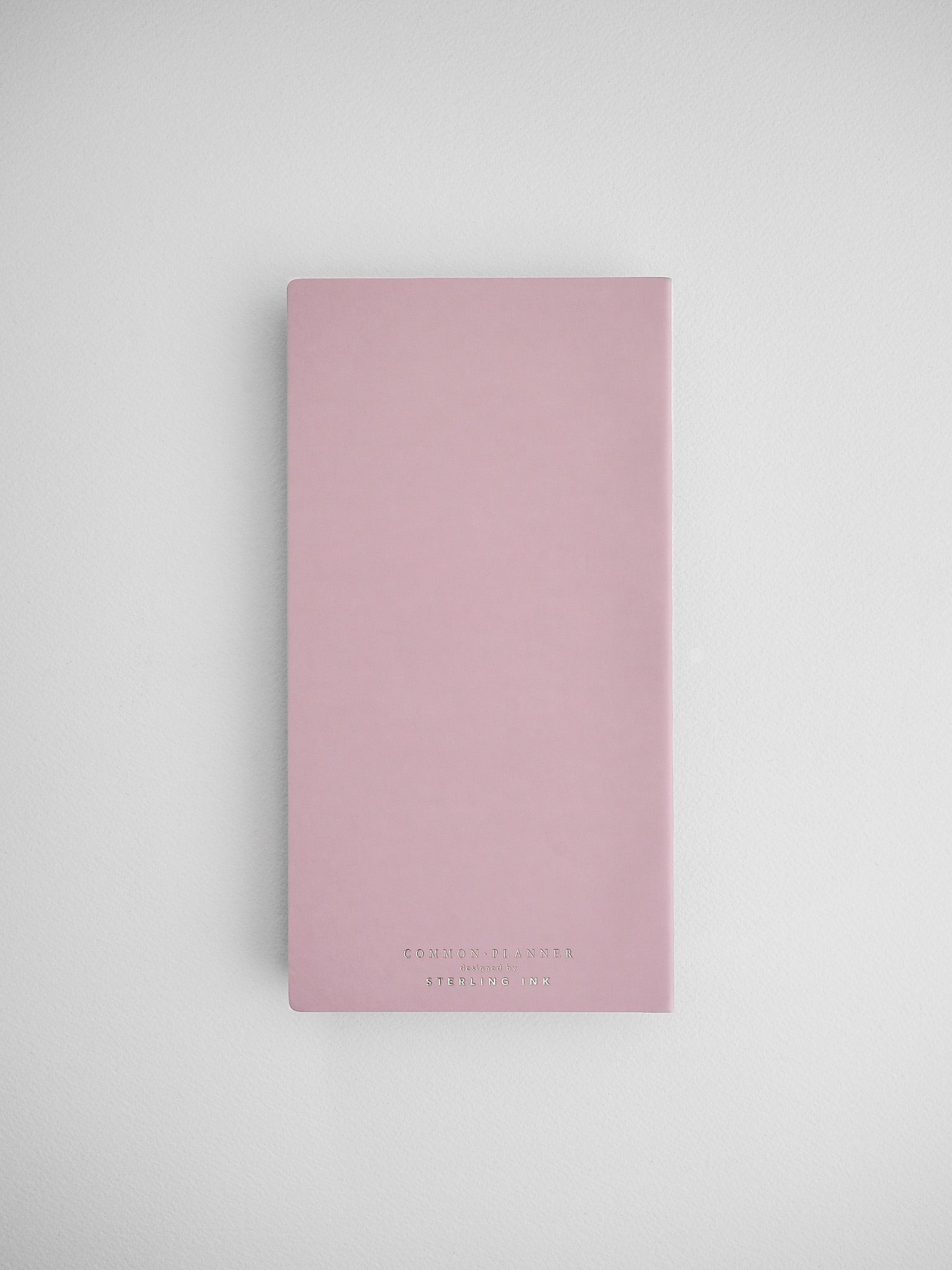 Soft blush pink common planner notebook cover, featuring minimalist black branding for an organized full-year journal.