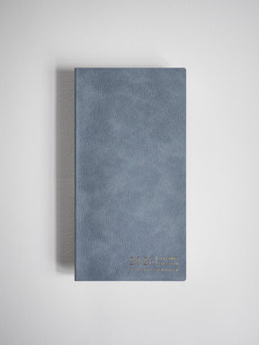 A compact, slate blue-gray planner cover featuring a subtle textured faux-leather finish and minimalist gold lettering of the year 2026 near the bottom center.