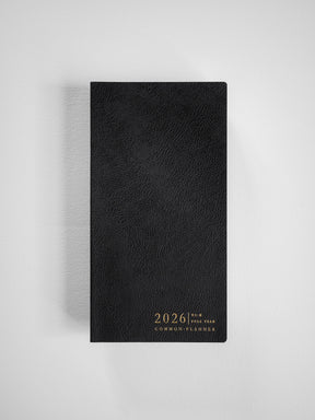Elegant black planner with a textured faux-leather cover, featuring metallic gold centered text that reads "2026 Full Year Common Planner."