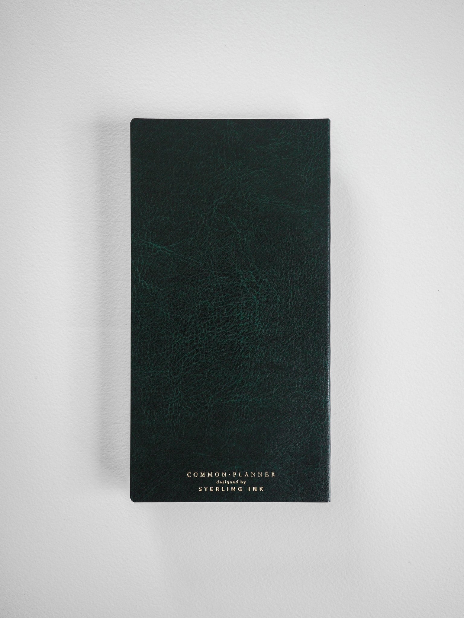 Dark forest green planner featuring a subtle textured faux leather finish and debossed gold lettering that reads 'COMMON PLANNER designed by STERLING INK'.