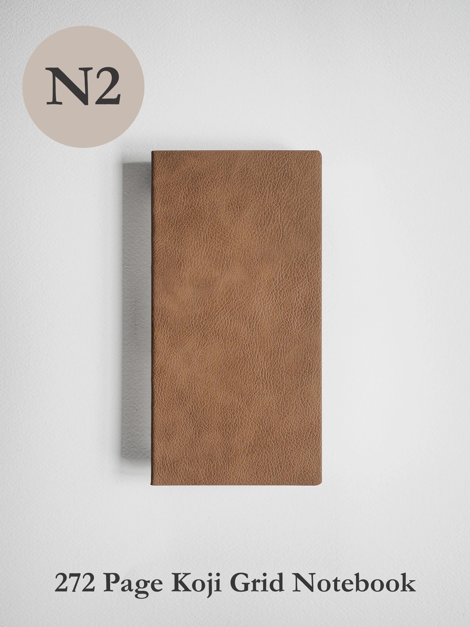 A brown textured notebook with a grid layout, shown vertically on a light gray background. A beige circle in the top-left corner contains the text 'N2', and the text '272 Page Koji Grid Notebook' is printed at the bottom.
#Color_Caramel