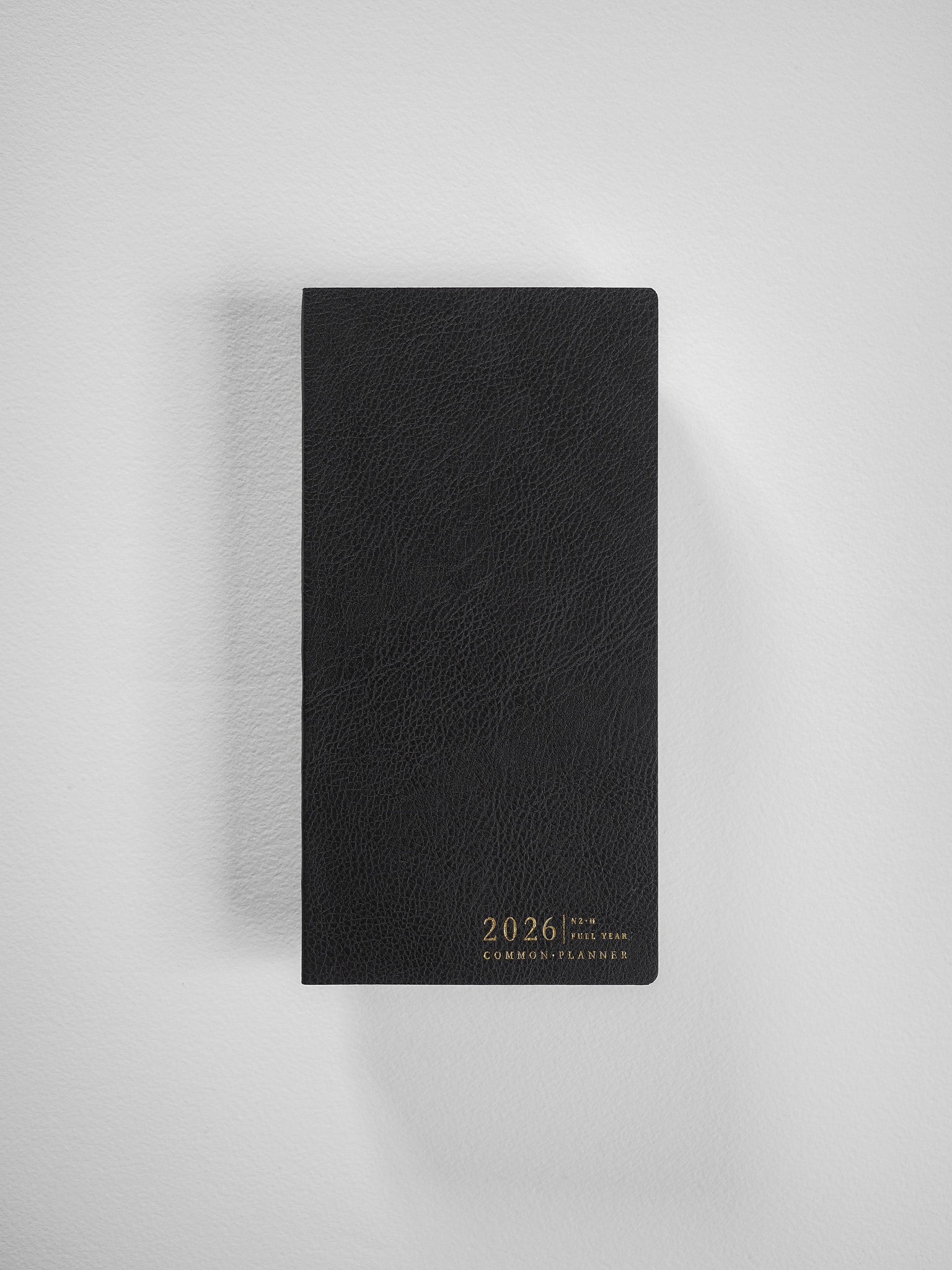 A sophisticated black, textured faux leather planner cover featuring centered debossed lettering that reads "2026 Common Planner" for organization.