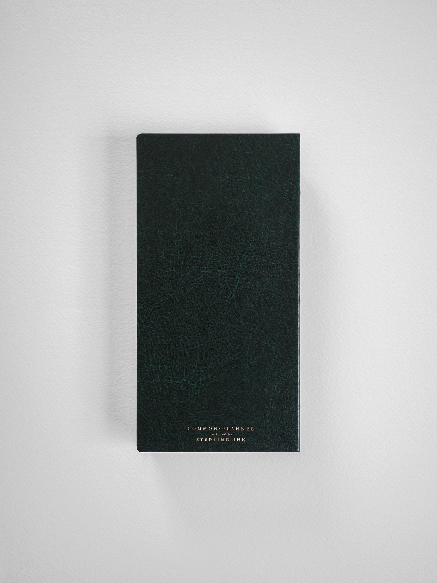 A compact, vertical planner featuring a deep charcoal, textured faux-leather cover, with centered white text branding for 'Common Planner' and 'Sterling Ink'.