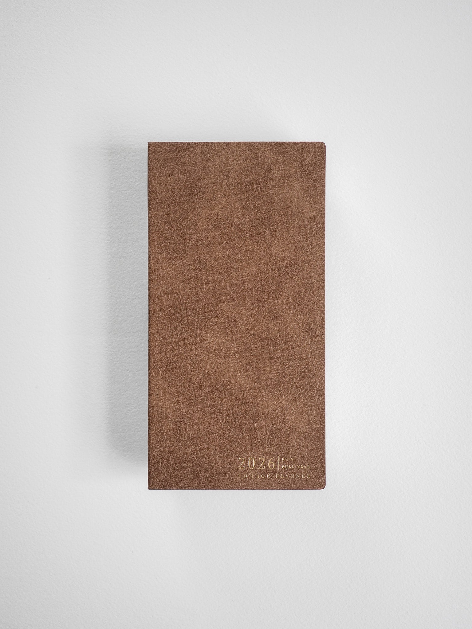 Rich, deep brown vertical planner cover with a faux leather texture, subtly debossed with "2026 Full Year Common Planner" in a minimalist design.