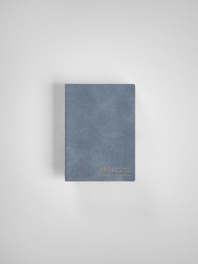 Slate blue compact planner with a textured cover, featuring embossed metallic gold lettering that highlights the year 2026.