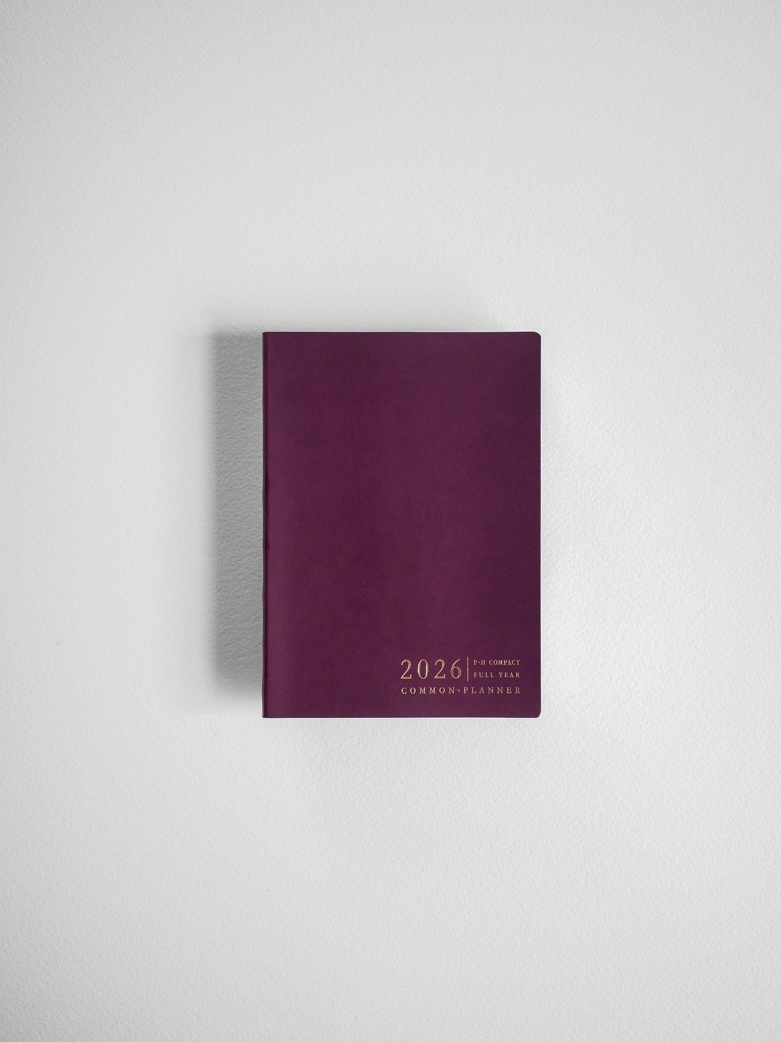 A compact, solid burgundy planner cover displaying white text detailing the "2026 P.H. Compact Full Year Common Planner."